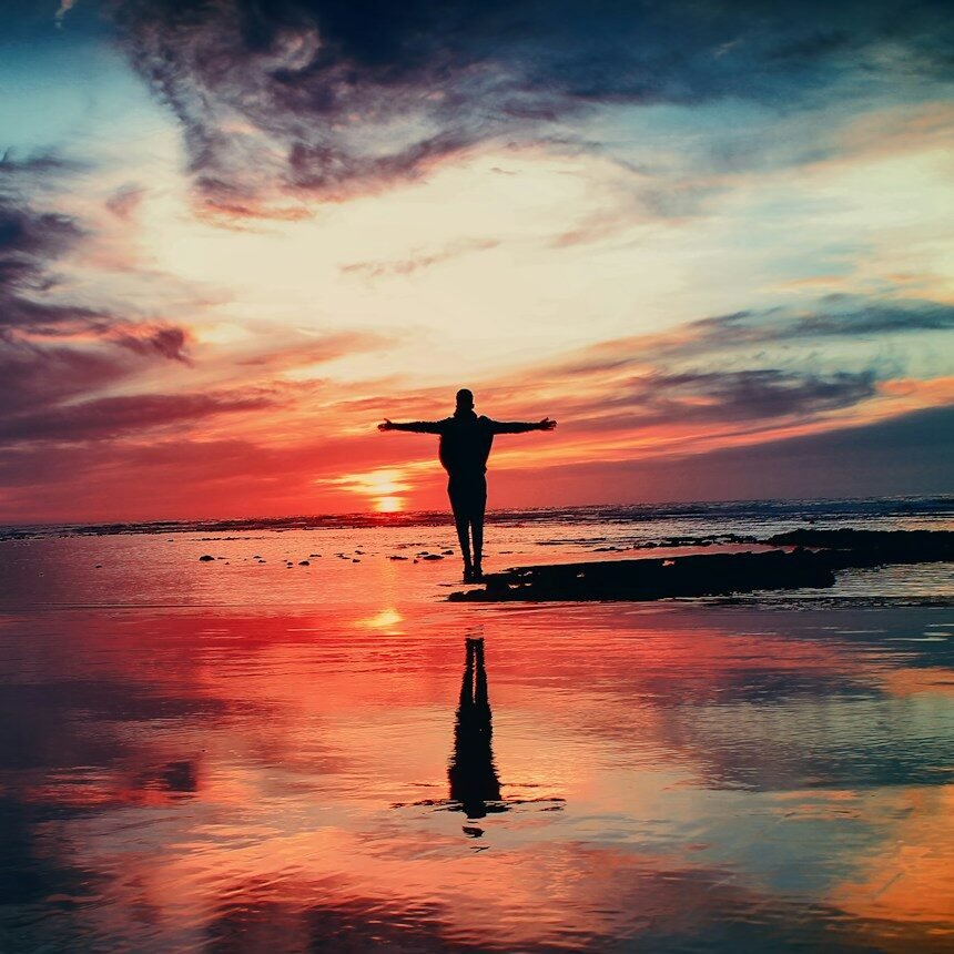 silhouette of person standing on rock surrounded by body of water